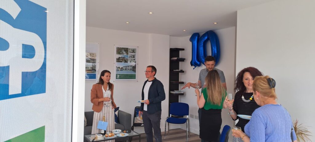 Sevenoaks Plans celebrating 10 years in business with connections and friends joining the celebrations. Door partly open showing people chatting and drinking champagne to celebrate.